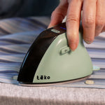 A close-up of a hand using a Teko portable steam iron on a striped blue and white shirt over a gray ironing board.