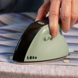 A close-up of a hand using a Teko portable steam iron on a striped blue and white shirt over a gray ironing board.